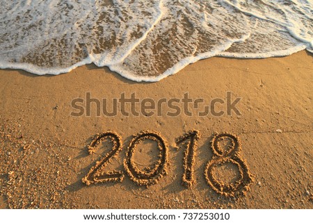 New Year 2018 is coming concept - inscription 2017 and 2018 on a beach sand, the wave is starting to cover the digits 2017 Royalty-Free Stock Photo #737253010