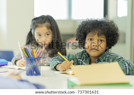 Little Chinese girl vs African boy sit in Kids library. Draw or paint kids pictures in recreation room with happiness. Teacher want kids imagine and develop their brains. Education supports activity.