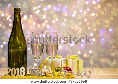 Bottle of champagne and glasses are placed together with a gift box and shiny balls. There is wooden texts "2018". Space on top right for your wording.