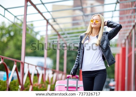 Blonde girl stands at the station with a suitcase pink