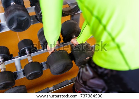 The hand of a strong man takes a heavy dumbbell in the gym