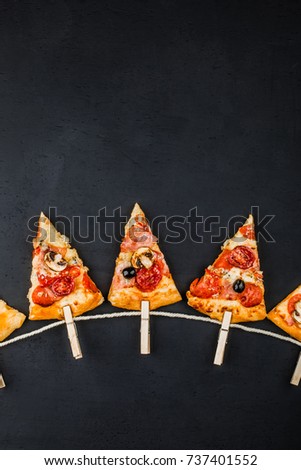 Slices of pizza in the form of a garland of flags on a dark background. Pizza menu. Conceptual space for text. Billet for the poster of pizzeria.