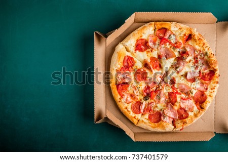 Pizza in a cardboard box on a green chalkboard background. Space for text. View from above. Pizza delivery. Pizza menu.