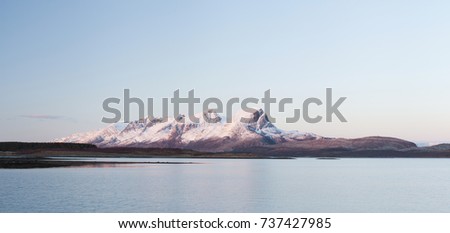 Panorama photo of snow-covered mountains in Norway on quiet evening, reflection on water. 