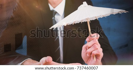 Businessman holding paper umbrella against blue background