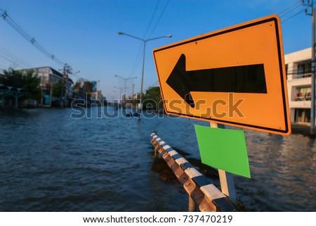 Traffic arrow sign and green board for copy space located on blurred flooding road with sunset light, Mega floods in Thailand, November 2011, image for Natural disaster / Transportation concept
