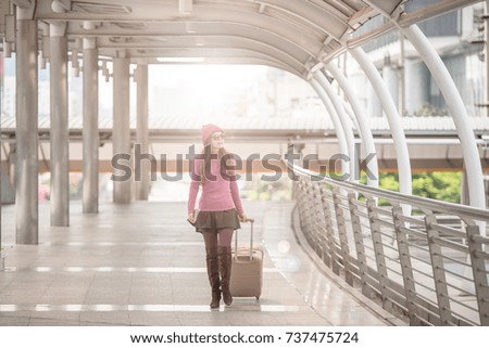 Portrait of a traveling young woman with luggage walking through the poles lined of international airport terminal