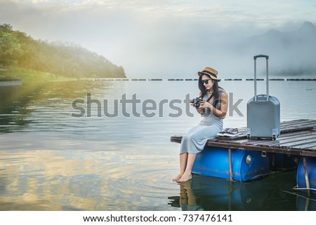 woman traveler have baggage taking photo for view of mountain lake and fog by camera on holiday.