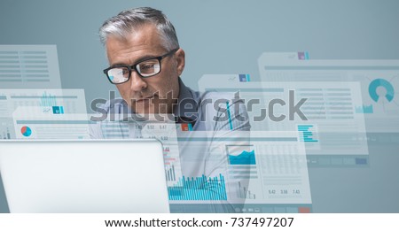 Businessman reading financial reports on visual screens and working with a laptop, finance and technology concept