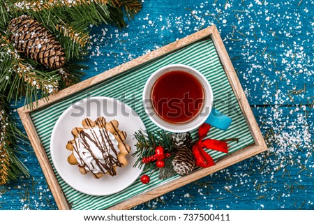 Photo of tray with mug of tea and cakes on table with spruce, snow and New Year decorations