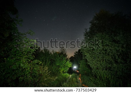 Rural road with a fiery track under the starry sky. Night landscape. The concept of a path, movement, purpose.