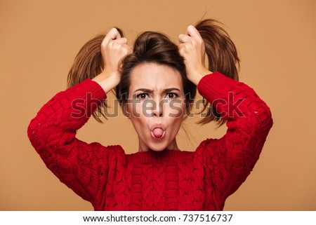 Picture of funny caucasian woman dressed in sweater standing isolated. Looking camera showing tongue.