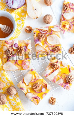 Pizza cut into pieces with a pear and onion on a white stand, top view, selective focus