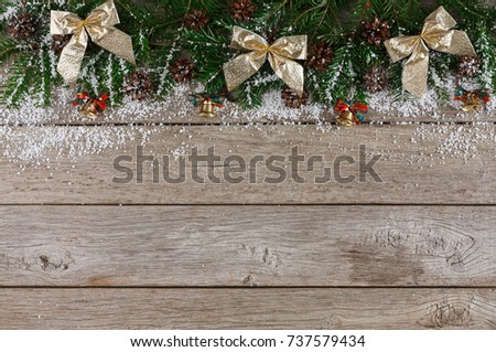 Christmas background with copy space, top view on pine tree twigs with pine cones, golden bows, bells and snow frame on wooden table. Xmas decorations, winter holidays concept
