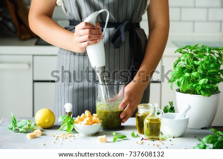 Woman using hand blender to make pesto. White kitchen interior design. Copy space. Vegetarian, clean eating lifestyle concept Royalty-Free Stock Photo #737608132