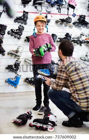 Male shop assistant helping boy to try on roller-skates in sports store
