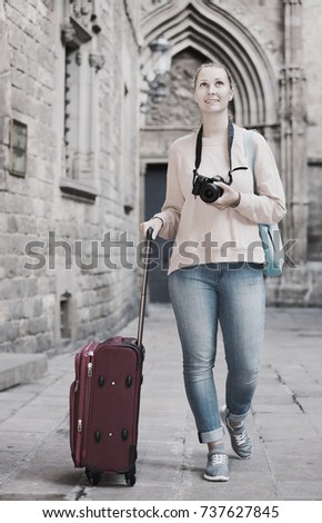 Young girl holding the camera in hands and photographing in a city