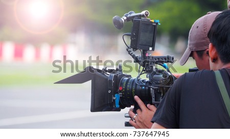 Blurry image of movie shooting or video production and film crew team with camera equipment at outdoor location and light flare effect.  Royalty-Free Stock Photo #737647945