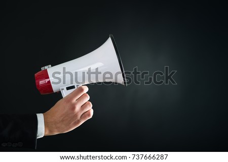 Close up of businessmans hand holding megaphone over dark background Royalty-Free Stock Photo #737666287