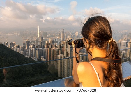 Young Asian beautiful girl take photo of Hong Kong skyline and Victoria harbor from the Peak in evening