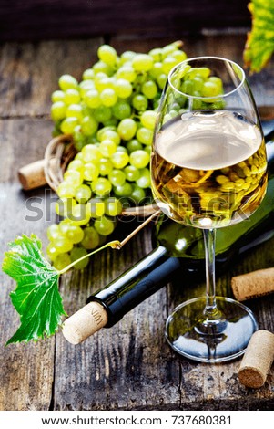 White wine in a glass with fall grapes, old wooden background