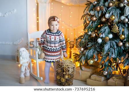 Beautiful little blond girl with brown eyes smiling at the New Year on the background of the Christmas tree