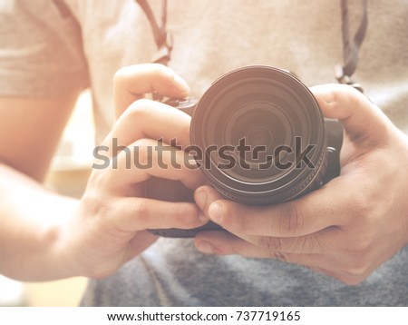 Photography or traveler Concept.The photographer hold black DSRL camera in his hands against building blur background and sunlight in summer season, selective focus. Vintage style.