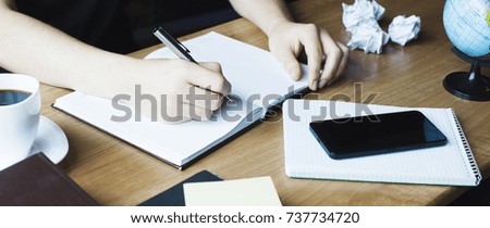 Beautiful Female hands with phone and cup of coffee write pen in a notebook of tasks and goals to work on a wooden table
