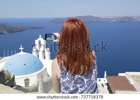Woman taking a picture of the blue dome Church St. Spirou in Firostefani on the island of Santorini, Greece