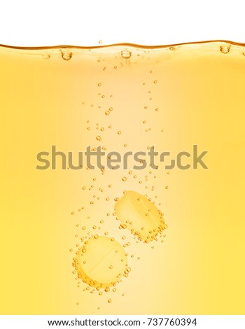 Two vitamins pills dissolves in yellow water close-up on white background