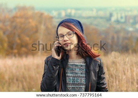 one teenage girl with red hair smiling and calling on the phone in nature. evening warm light autumn season. general view of the background view far away city