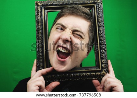Young man with picture frame filled with excitement. Man on chroma key, emotions green background. Man holding a vintage frame
