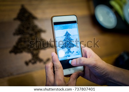 A man take a picture by smartphone of christmas tree made from roasted coffee beans on wood table.