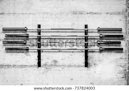 Four barbell weight bars on the stand screwed on the grunge wall prepared for bodybuilding weightlifting sport in the gym black and white high contrast Royalty-Free Stock Photo #737824003