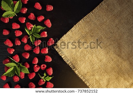 Many tasty raspberries with leaves on black stone background, delicious first class organic fruit as a concept of summer vitamins