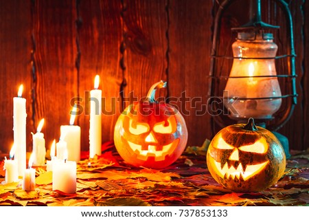 Halloween pumpkin with glowing face on a wooden background with many flaming candles, an antique lantern and autumn leaves. Idea for flyers, poster, placard, billboard