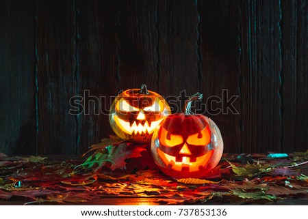 Halloween pumpkin with glowing face on a wooden background with autumn leaves. Idea for flyers, poster, placard, billboard. Free space