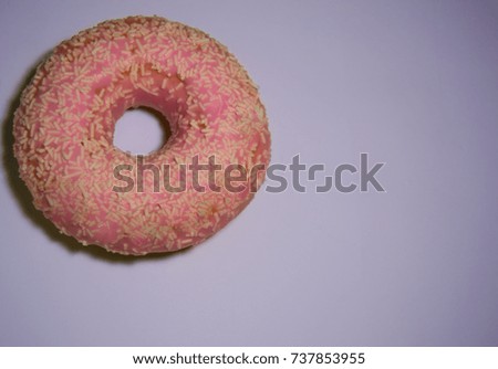 Pink icing donut with sprinkles or toppings isolated in colorful purple background.  Unhealthy nutrition and sugar and sweet concept..