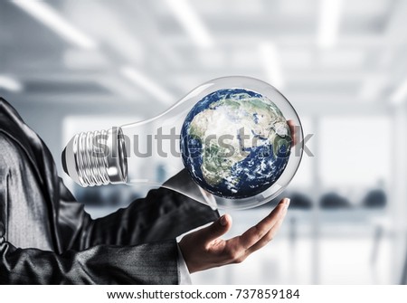 Closeup of business woman in suit holding in hands lightbulb with Earth globe inside with office view background. Elements of this image are furnished by NASA
