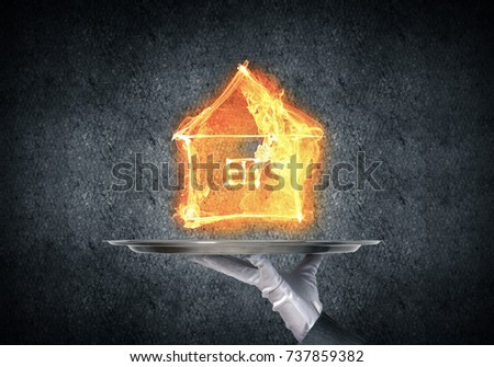 Cropped image of waitress's hand in white glove presenting flaming house symbol on metal tray with dark wall on background.