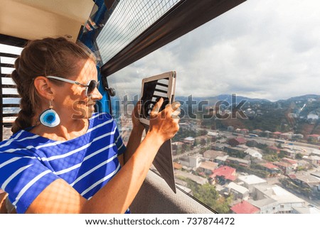 a young girl takes a photograph of a tablet while traveling on a cable car