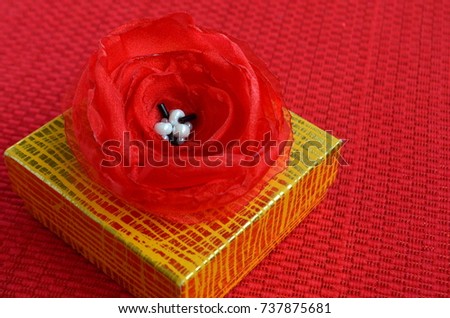 Yellow and golden gift box with a large red rose flower on top with copy space on deep red background.  Gift-wrapped box. Celebration, birthday, anniversary, Christmas, holiday theme.