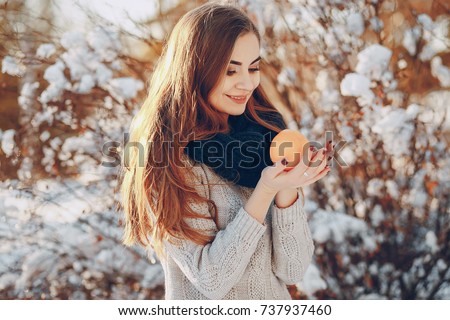girl getting ready to eat an orange while walking in a park full of snow