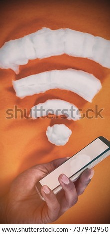 Cropped hand holding mobile phone by wifi icon on orange background