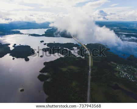 Beautiful view from a road going through the beautiful lake and forest, surrounded with water on both sides, shot above from drone, aerial vibrant picture, Murmansk Oblast, Russia