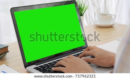 Over the shoulder shot of a woman typing on a computer laptop with a key-green screen. Woman hand typing  laptop with green screen.