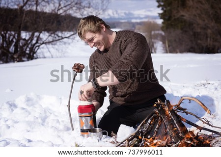 a man cooks sausages on a stick at the campfire in winter forest Royalty-Free Stock Photo #737996011
