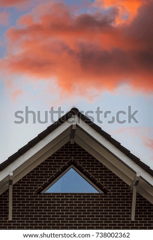 Light pink clouds in the rays of the sunset over the roof of the house.