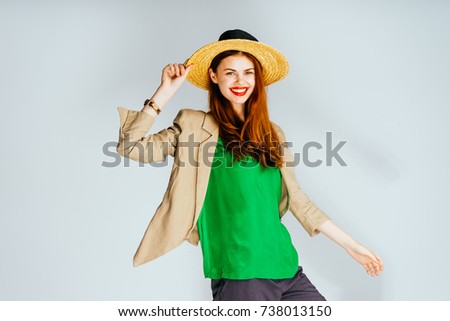 a girl with red lips and in a bright green blouse holds her hat with her hand and laughs