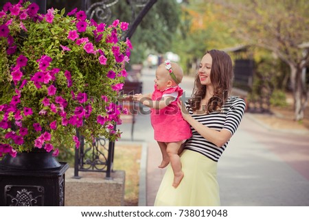 Picture of young lady brunette mother in soft zebra shirt and ivory colour skirt happy playing with baby daughter on city streets park close to pink rose flowers summer time child.
